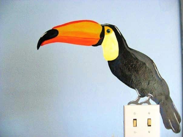 A jungle mural featuring a toucan sitting on a light switch, painted by Adrienne of AboutMurals.ca