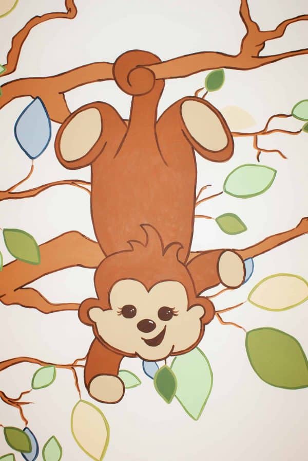 A monkey hangs from tree branches in this hand-painted mural created by Adrienne of AboutMurals.ca