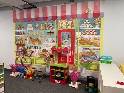Bakery Wall Mural, as seen in this Preschool at Batter Zone in Hamilton, Ontario, is a kids wallpaper of a bakery shop selling cake, pastries, cookies, cupcakes, croissants and bread from About Murals.