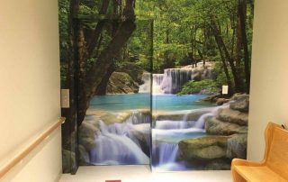 Erawan Waterfalls Thailand Wall Mural, as seen in this hospital, features a turquoise river flowing over rocks in a forest. Forest wallpaper sold by AboutMurals.ca.