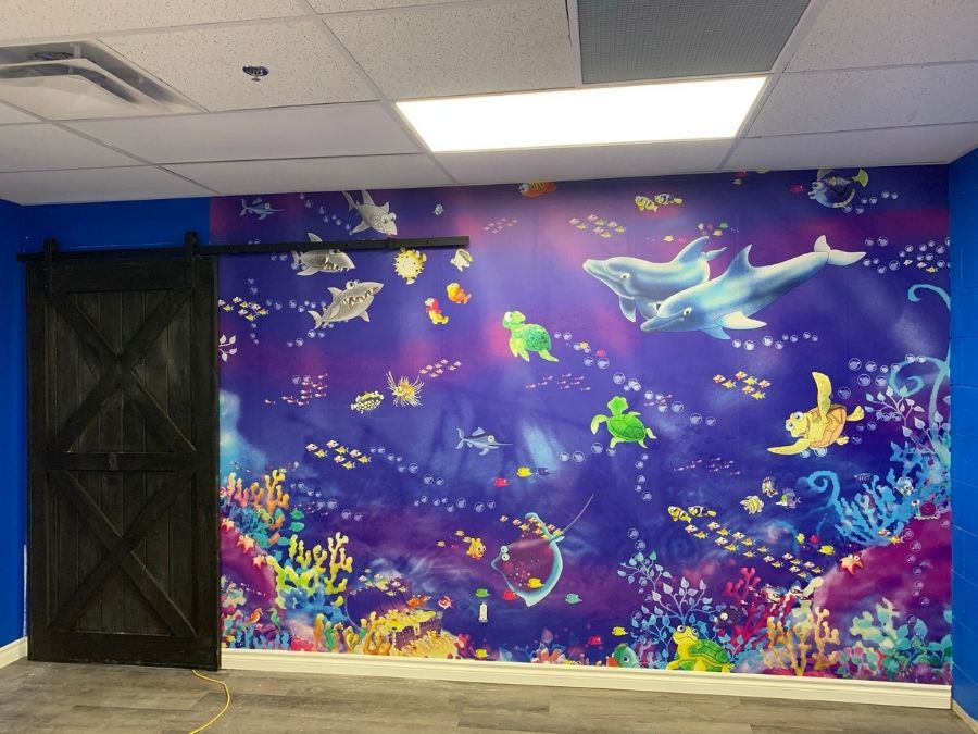 Fish Wall Mural, as seen at an indoor playground, is an underwater wallpaper for kids with dolphins, sharks, turtles, fish and colourful coral from About Murals.
