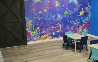 Fish Wall Mural, as seen on the wall of this party room, is a kids wallpaper featuring cute under the sea characters like a fish, shark, turtle, dolphin, sting ray and star fish swimming in colorful coral from About Murals.