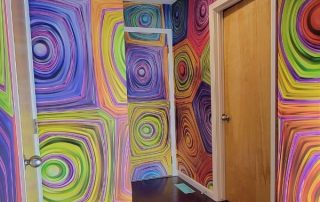 Hypnosis Wall Mural, as seen on the walls of this hallway, is a geometric wallpaper with colorful hypnotic swirls from About Murals.