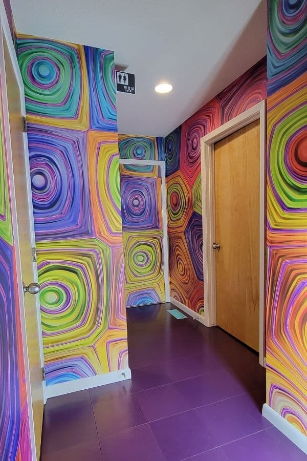 Hypnosis Wall Mural, as seen on the walls of this hallway, is a geometric wallpaper with colorful hypnotic swirls from About Murals.