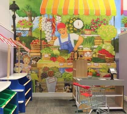 Market Place Wall Mural, as seen in this preschool, is a children’s wallpaper with fruit and vegetables labeled with words for easy reading from About Murals.