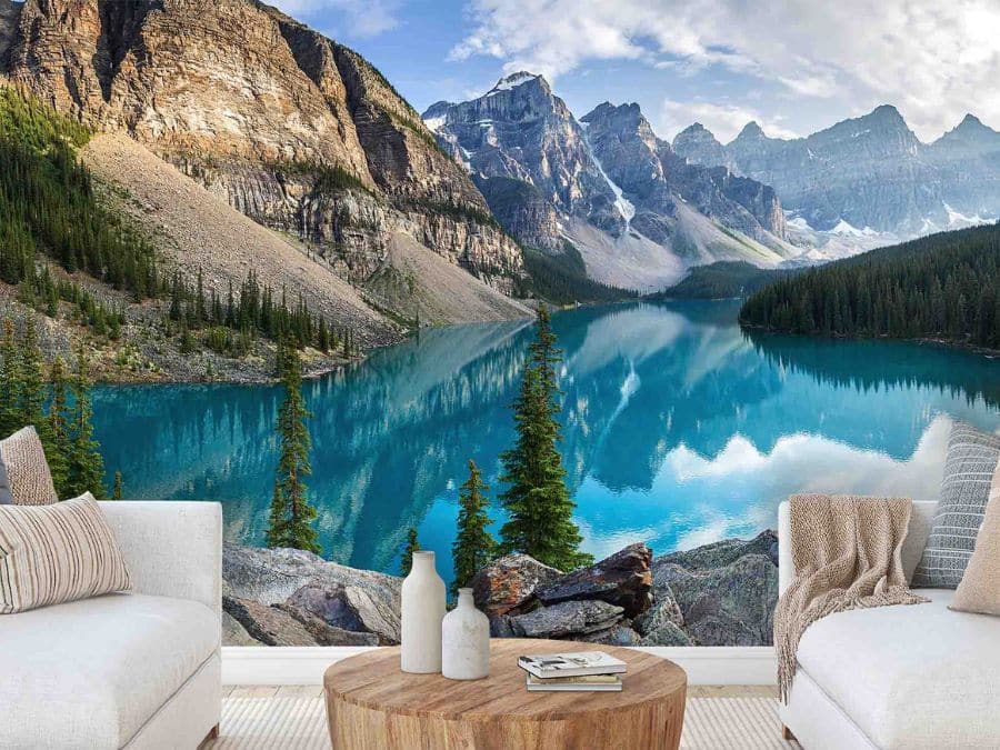 Moraine Lake Wallpaper, as seen on the wall of this living room, is a landscape mural of Alberta mountains at sunset overlooking a blue lake from About Murals.