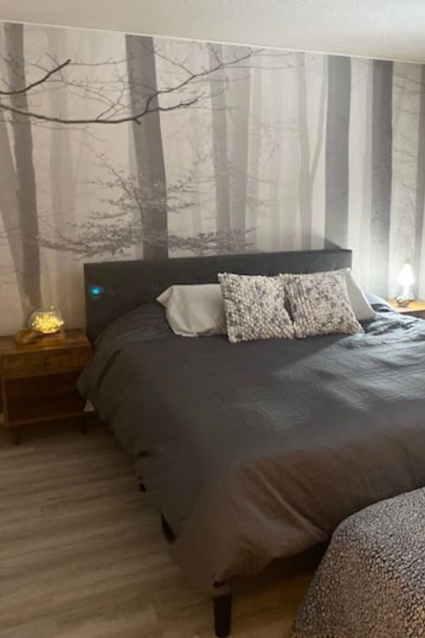 Morning Fog Wallpaper, as seen on the wall of this grey bedroom, is a wallpaper mural with a beautiful forest scene of misty grey trees from About Murals.