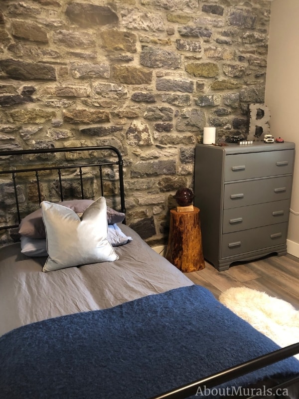 Stone Wall Mural, as seen in this bedroom, features a wall of realistic, textured grey, blue and yellow stacked stones that almost looks 3D. Stone wallpaper sold by AboutMurals.ca.