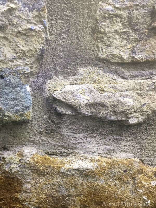 A close-up view of Stone Wall Mural features textured, 3D looking blue, mossy yellow and grey stones. Stone wallpaper sold by AboutMurals.ca.