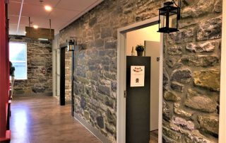 Stone Wall Mural, as seen in this hallway, features grey stacked stones with hints of blue, purple and yellow. Stone wallpaper sold by AboutMurals.ca.