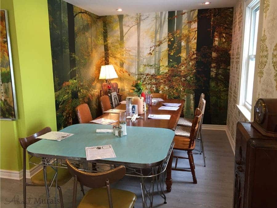 Sunny Autumn Wallpaper, as seen on the wall of this retro restaurant, is a photo mural of sunshine beaming through orange and yellow trees in a forest from About Murals.