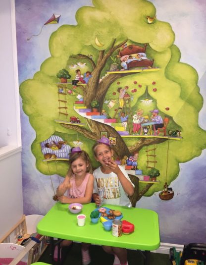 Tree House Wall Mural, as seen in this indoor play place, is a children’s wallpaper featuring kids playing and having fun in a colorful tree from About Murals.