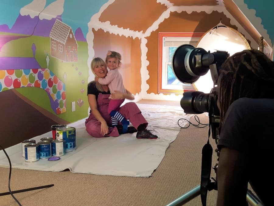 Adrienne Scanlan sits in front of her Candy World Mural with daughter in front of photographer