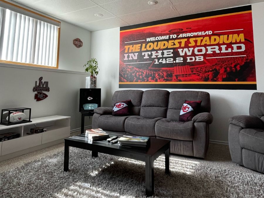 Custom Printed Wallpaper, as seen on the wall of this living room, is a Chiefs mural of Arrowhead Stadium with the words "The Loudest Stadium in the World" from About Murals.
