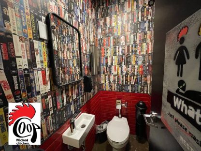 Custom Wallpaper, as seen on the wall of the Coop Wicked Chicken Restaurant, of VHS tapes from the 90s in a bathroom from About Murals.