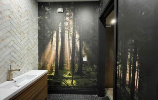 This custom wallpaper, as seen on a bathroom wall in Movengo's corporate office in Hamilton, Ontario, is a forest wallpaper with sunbeams shining through dark trees from About Murals.