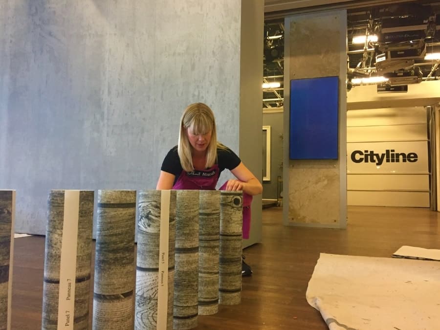 Adrienne offers wallpaper installation as part of her services, as seen on set at Cityline while hanging a wood wallpaper.