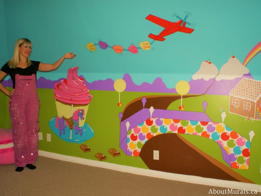 A candy mural, painted by Adrienne of AboutMurals.ca, features a cupcake carousel, airplane totting sweet tart candy, bubble gum bridge, ice cream mountains, flowing chocolate river and gingerbread house.