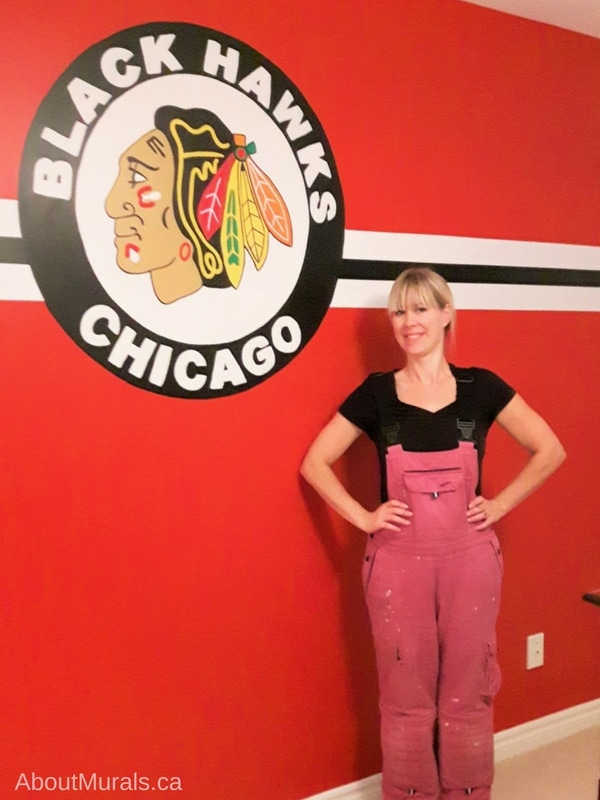 Muralist, Adrienne of AboutMurals.ca, stands next to a Chicago Blackhawks mural she painted