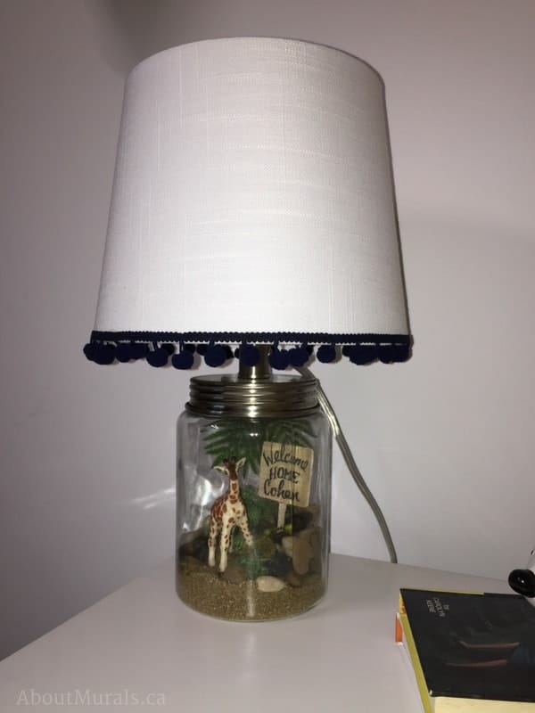 A custom lamp featuring a giraffe with rocks, leaves and a sign saying "welcome home Cohen" created by Sherry Holmes for Holmes Next Generation.