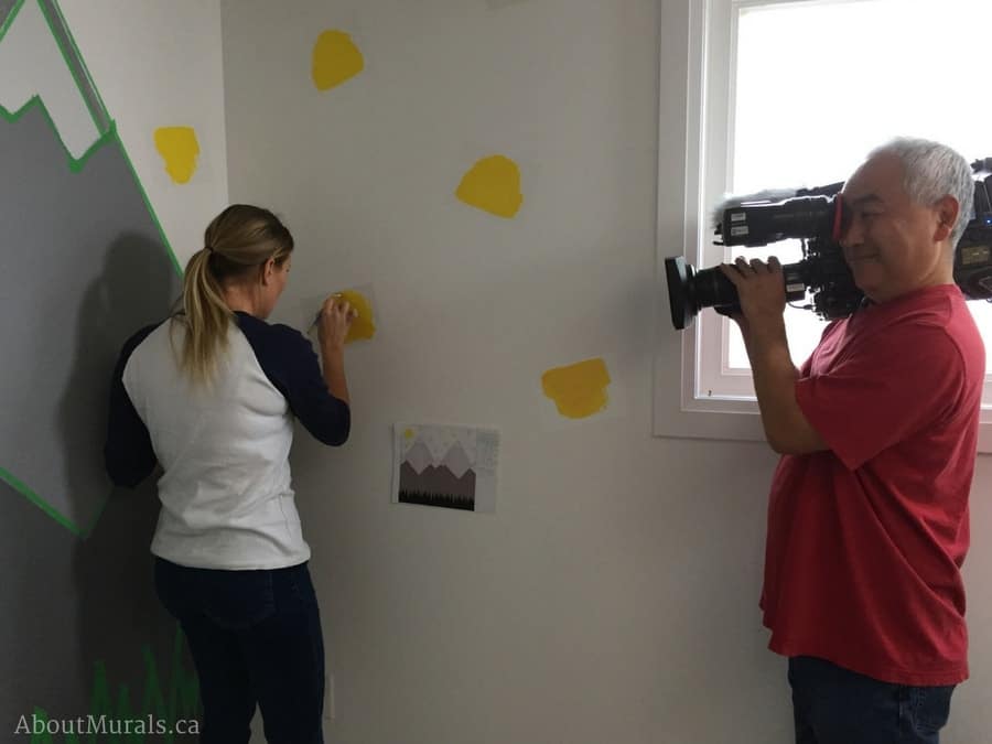 Sherry Holmes learns how to paint yellow triangles and a mountain mural with Adrienne of AboutMurals.ca for the Holmes Next Generation TV show