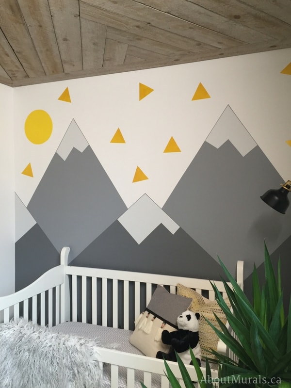 A mountain mural nursery painted by Adrienne of AboutMurals.ca for the Holmes Next Generation TV show sits behind a baby's crib