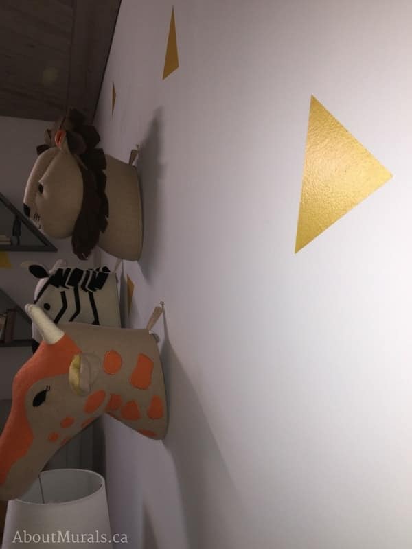 A shimmery triangle painted by Adrienne of AboutMurals.ca on the walls of a baby nursery, along with stuffed animal heads.