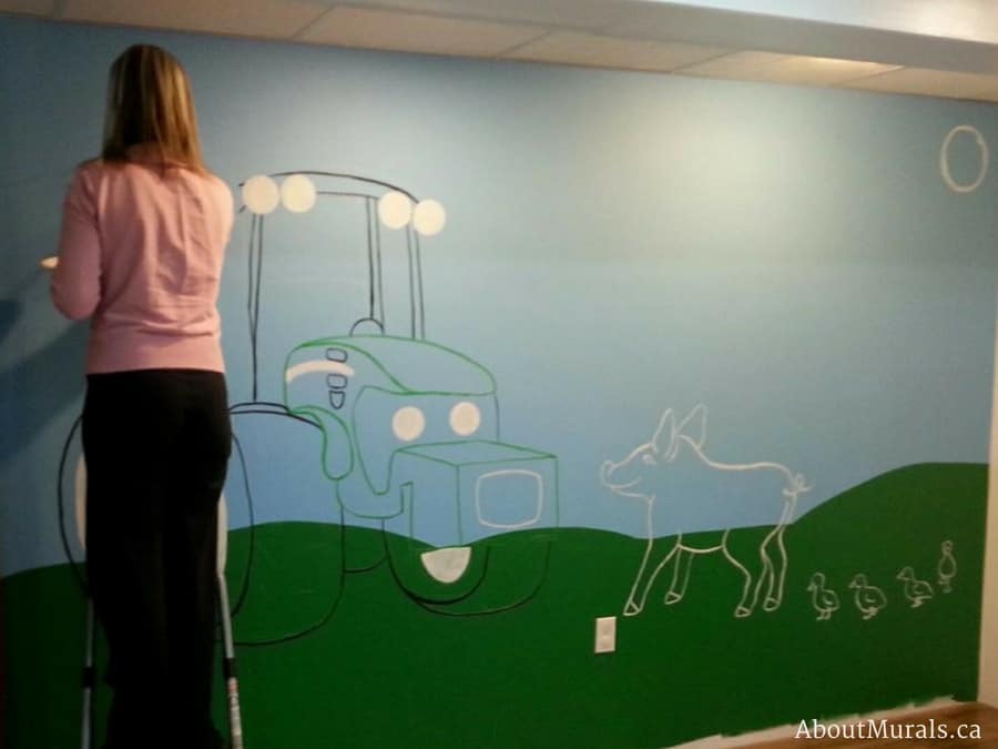 Muralist, Adrienne of AboutMurals,ca, paints a tractor mural in a playroom