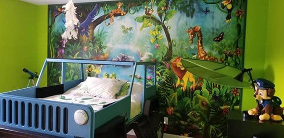 A kids jungle wallpaper sits behind a jeep bed in a boy's room, sold by AboutMurals.ca