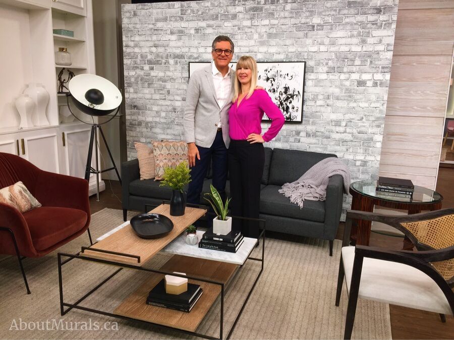 Brian Gluckstein stands with Adrienne of AboutMurals.ca in front of her gray brick wallpaper on set at Cityline