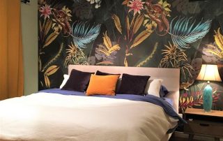 Black Tropical Wallpaper, as seen on this bedroom wall, features exotic flowers, palm leaves, banana leaves and lizards on a dark background. Tropical wallpaper sold by AboutMurals.ca