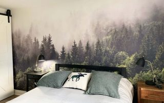 Foggy Forest Wallpaper, as seen on the wall of this bedroom, is a photo mural of mist settled into the tops of pine trees from About Murals.