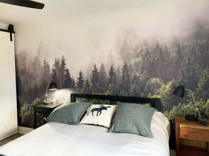 Foggy Forest Wallpaper, as seen on the wall of this bedroom, is a photo mural of mist settled into the tops of pine trees from About Murals.