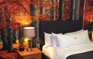Red Forest Wallpaper, as seen on the wall of this bedroom, features grey trees with red autumn foliage from About Murals.