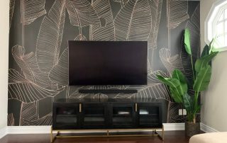Black and Gold Leaf Wallpaper, as seen on the wall of this modern living room, is a tropical mural with banana leaf silhouettes on a dark background from About Murals.