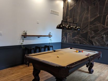 Black and Gold Leaf Wallpaper, as seen on the wall of this pool hall, is a tropical wall mural with a gold banana leaf outline pattern on a dark background from About Murals.