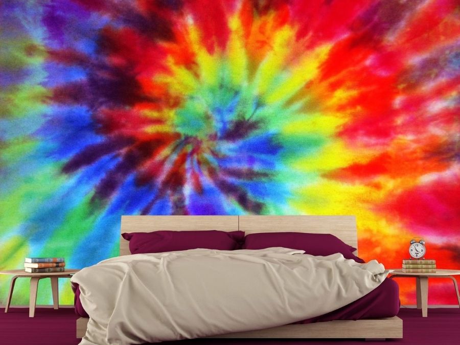 Rainbow Tie Dye Wallpaper, as seen on the wall of this colourful bedroom, features a multi-colour spiral on a fabric textured background from About Murals.