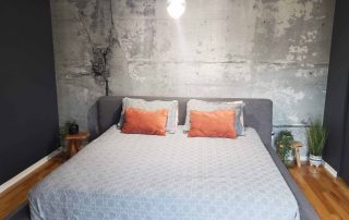 Cracked Concrete Wallpaper, as seen on the wall of this industrial bedroom, is a photo mural of a textured concrete wall from About Murals.