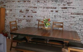 Distressed Brick Wallpaper, as seen on the wall of this dining room, features decaying white paint over red brick from About Murals.
