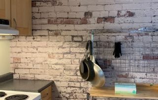 Distressed Brick Wallpaper, as seen on the wall of this kitchen, is a high resolution photo mural with white paint decaying on red brick from About Murals.