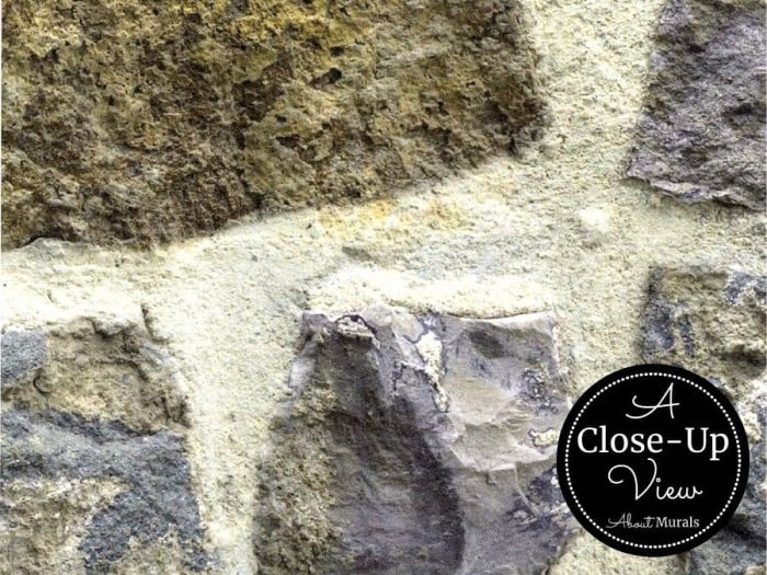 A close-up view of a moss green and light blue field stone in a country stone wallpaper from About Murals.