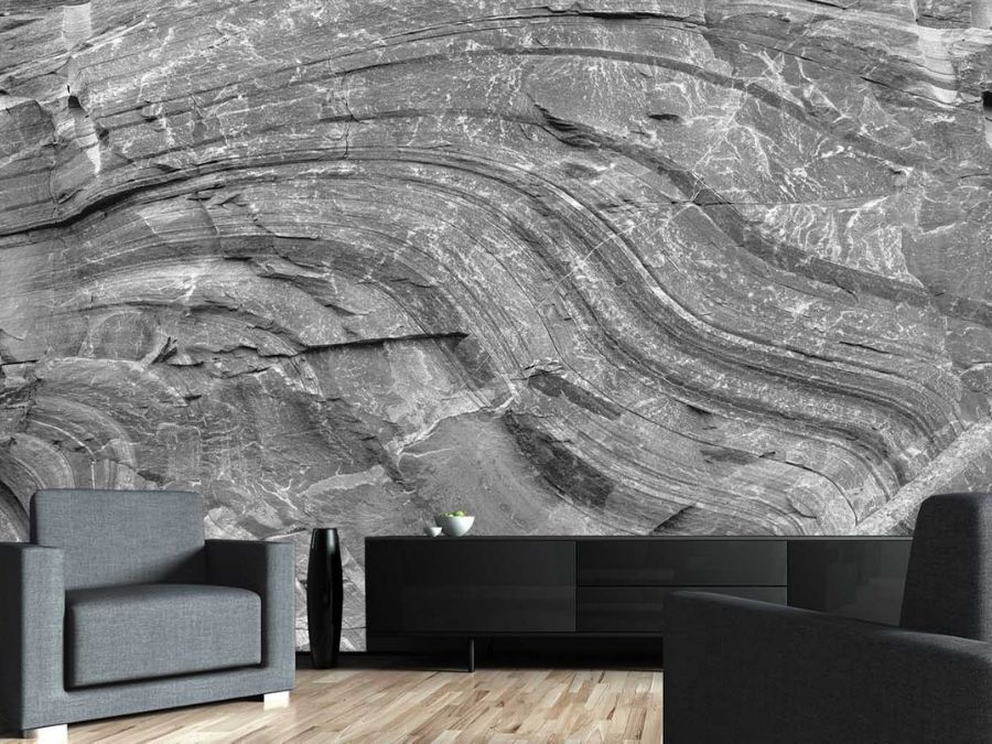 Gray Rock Wallpaper, as seen on the wall of this living room with black sofas, is a photo mural of a rock face wall from About Murals.