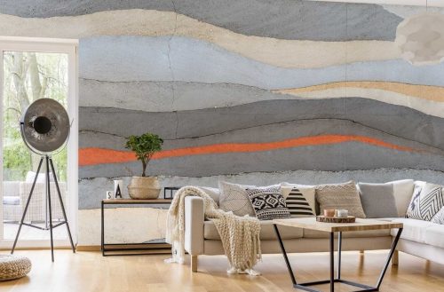 Grey and Orange Concrete Wallpaper, as seen on the wall of this grey and orange living room, is a photo mural of a concrete wall with layers of grey, orange, yellow and light blue from About Murals.