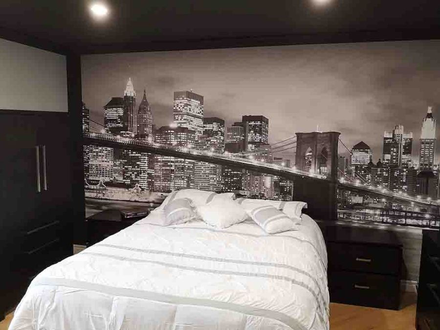 Brooklyn Bridge Park Wallpaper, as seen on the wall of this dark bedroom, is a sepia photo mural of the New York suspension bridge at night with skyscrapers overlooking the East River from About Murals.