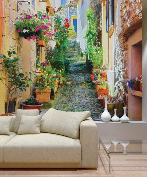 French Village Wallpaper, as seen on the wall of this living room, is a photo mural of a flower lined, cobblestone street in Collobrieres, Provence, France from About Murals.