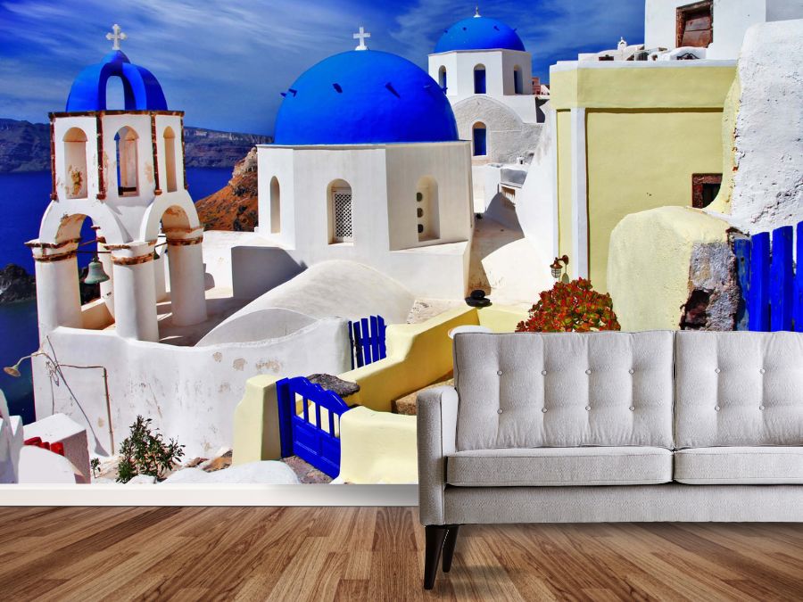 Greece Wallpaper, as seen on the wall of this living room, is a photo mural of blue and white buildings in Oia, Santorini from About Murals.