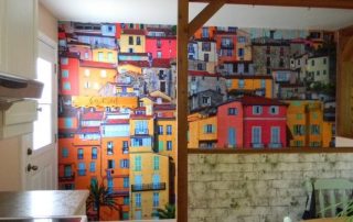 Menton Wallpaper, as seen on the wall of this kitchen, is a photo mural of colorful houses in a Mediterranean commune in France from About Murals.