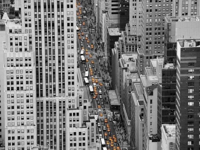 NYC Street Wallpaper is an aerial black and white photo mural of cars, buses and yellow cabs driving between tall buildings in New York City from About Murals.