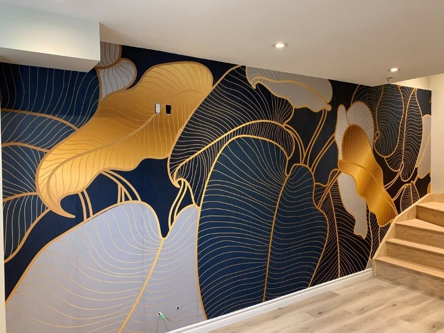 Philodendron Wallpaper, as seen on the wall in this basement, is a tropical mural with blue, teal and gold leaves from About Murals.