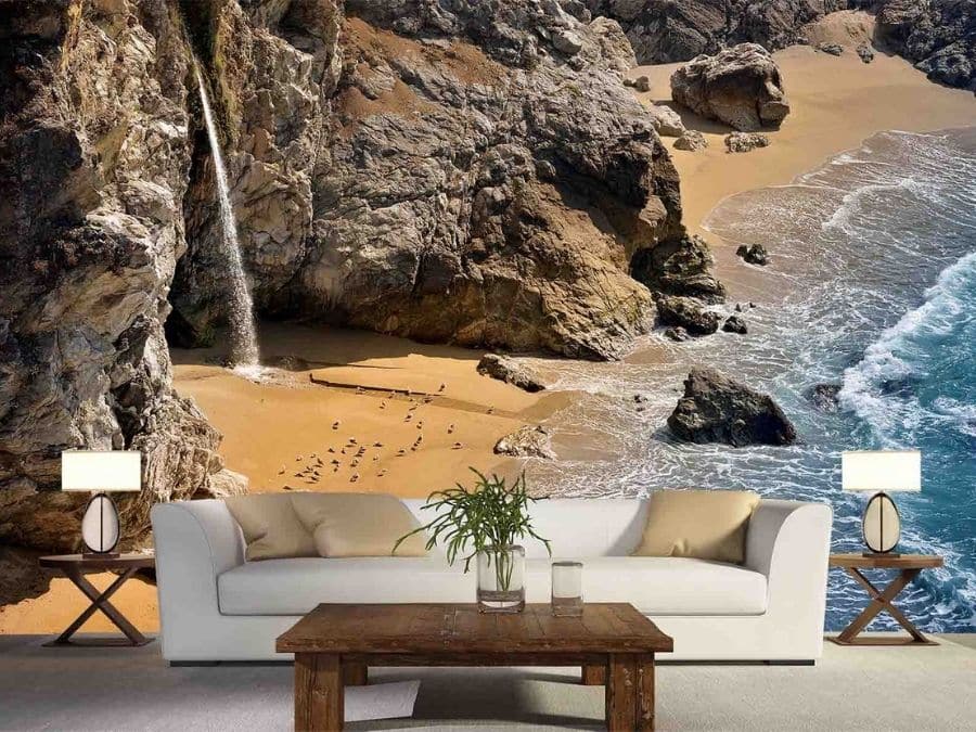 Big Sur Beach Wallpaper, as seen on the wall of this living room, is a photo mural of McWay Falls on Pfeiffer Beach in California from About Murals.